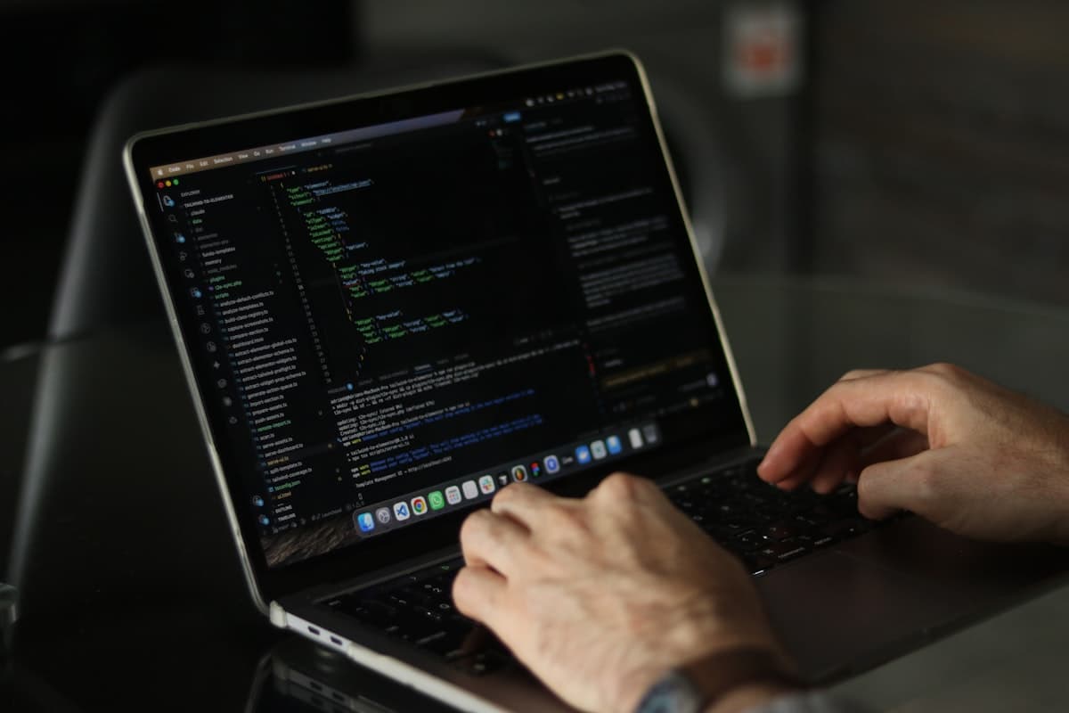 Developer reviewing code on a laptop in a dark workspace.